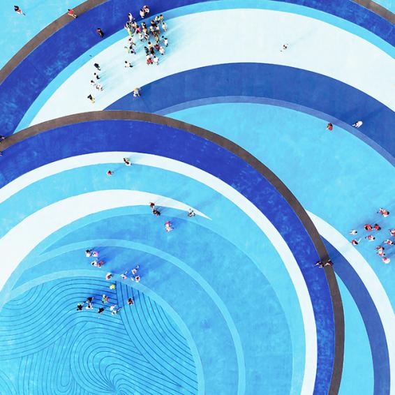 A blue swimming pool filled with people enjoying a sunny day, some swimming and others relaxing at the edge.